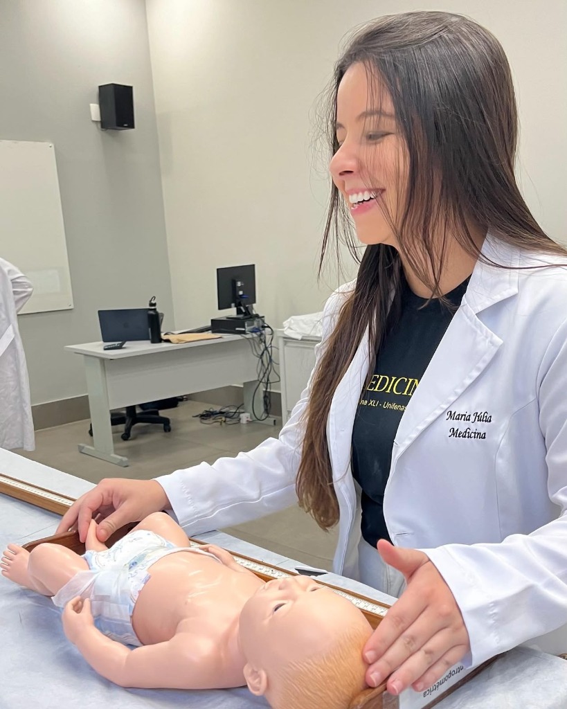 Maria Júlia cuidando com carinho de manequim infantil na aula prática de medicina na UNIFENAS